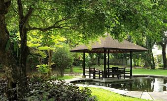 a serene park with a gazebo , surrounded by lush green grass and trees , creating a peaceful atmosphere at Royal Ambarrukmo Yogyakarta