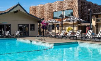 a large outdoor swimming pool surrounded by lounge chairs and umbrellas , with a building in the background at Red Lion Hotel Port Angeles Harbor
