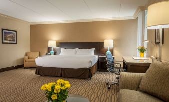 a large bed with white linens is in a hotel room with two lamps , a couch , and a vase of yellow flowers at Best Western Plus Strongsville Cleveland