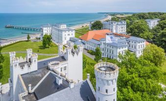 a large white building with a red roof and a brick tower is surrounded by trees and overlooks the ocean at Grand Hotel Heiligendamm - the Leading Hotels of the World