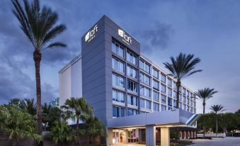 "a modern hotel building with the name "" international club "" on top , surrounded by palm trees and a clear blue sky" at Aloft Miami Dadeland