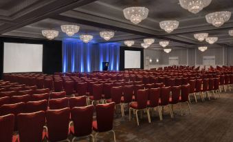 a large conference room with rows of red chairs and a screen at the front at Marriott Boston Quincy