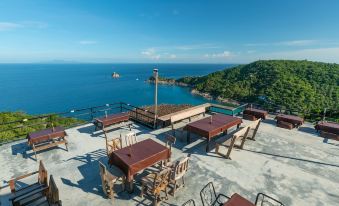 a rooftop terrace with wooden tables and chairs overlooking the ocean , creating a serene atmosphere at Taatoh Seaview Resort