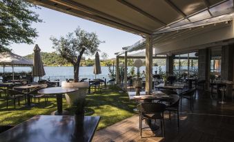 a restaurant with a view of a lake , surrounded by tables and chairs , and umbrellas providing shade at Hotel l'Approdo