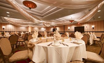 a large dining room with multiple tables covered in white tablecloths and chairs arranged around them at Wyndham Minneapolis South/Burnsville