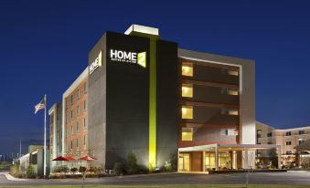 a large hotel with a yellow and black exterior is shown at night , surrounded by grass and trees at Home2 Suites by Hilton Oxford