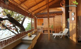 a wooden house with a thatched roof , surrounded by trees and overlooking the ocean , featuring a covered patio area with outdoor furniture at Chareena Hill Beach Resort