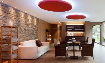 a modern living room with a white couch , wooden dining table , and red circular lights on the ceiling at Hotel Hubertus - Au Bregenzerwald