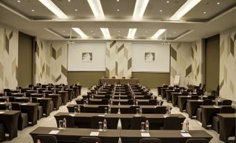 a large conference room with rows of tables and chairs , a projector screen at the front , and patterned walls at Mambruk Hotel & Convention