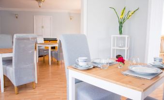 a dining room with a white dining table and chairs , along with a kitchen area at The Coast House B&B