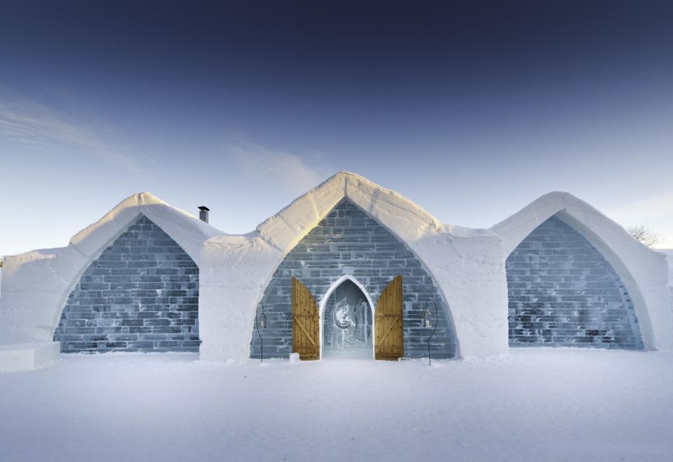 a large , snow - covered building with a blue and white exterior and a door , surrounded by snow at Hôtel de Glace