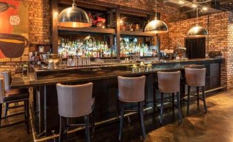 a modern bar with a brick wall , wooden counter , and three pink chairs surrounding it at Dakota Edinburgh