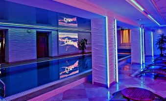 a luxurious indoor swimming pool with purple lighting , surrounded by sun loungers and palm trees at Metropol Hotel