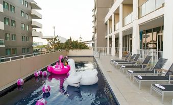 a large swimming pool with a pink flamingo float and white swan floaties in the water at Sage Hotel Wollongong
