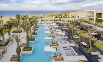 a long , narrow pool is surrounded by palm trees and lounge chairs on a beach at Nobu Hotel Los Cabos