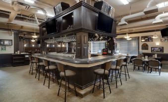 a modern bar with a large screen tv , multiple rows of chairs and stools , and an elegant counter at Best Western High Road Inn