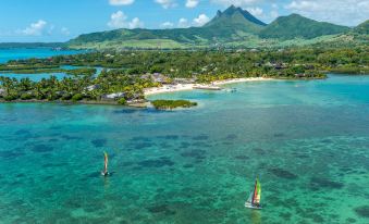 aerial view of a tropical island with two sailboats floating in the clear blue ocean , surrounded by lush greenery and mountains at Four Seasons Resort Mauritius at Anahita