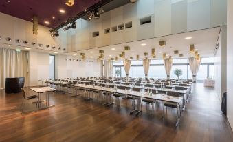 a large conference room with rows of tables and chairs , a stage at the front , and wooden floors at Belvoir Swiss Quality Hotel