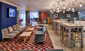 a modern lounge area with wooden floors , blue walls , and multiple couches , chairs , and tables at Holiday Inn Leeds - Garforth