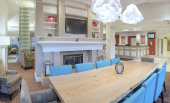 a large dining table surrounded by blue chairs in a room with a fireplace and a television at Hilton Garden Inn Plymouth