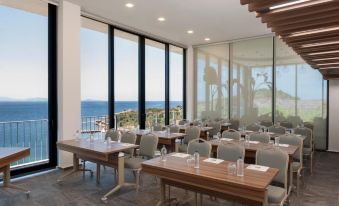 a conference room with wooden tables and chairs , large windows , and a beautiful view of the ocean at Le Méridien Bodrum Beach Resort