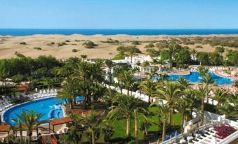 a beautiful resort with a large pool surrounded by lush greenery and palm trees , overlooking the ocean at Hotel Riu Palace Oasis
