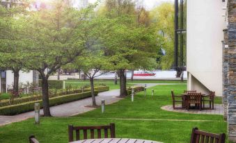 a well - maintained green lawn with a table and chairs placed in the middle , surrounded by trees and benches at Novotel Queenstown Lakeside