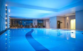 an indoor swimming pool with blue water , surrounded by a hotel lobby , and illuminated by ceiling lights at Crowne Plaza Reading East