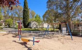 a playground with various play equipment , including swings and slides , in a sunny outdoor setting at Discovery Parks - Jindabyne