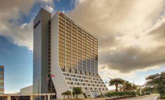 a modern building with a unique architectural design , surrounded by palm trees and under a cloudy sky at Mobile Marriott