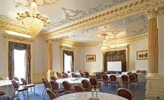 a large , ornate room with round tables and chairs is set up for a meeting at Avisford Park Hotel