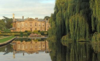 a large building is reflected in a body of water with trees and a willow tree at Coombe Abbey Hotel