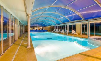 an indoor swimming pool surrounded by a glass enclosure , with several lounge chairs placed around it at Lagrange Vacances le Hameau de Peemor PEN