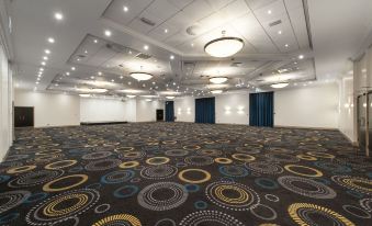 a large , empty conference room with a carpeted floor and multiple chandeliers hanging from the ceiling at Mercure Telford Centre Hotel
