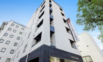 a tall white building with a red sign on the side , located in a city setting at Hotel Wing International Himeji