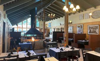 a large , well - lit restaurant with multiple dining tables and chairs , as well as a fireplace in the background at Shasta Inn