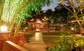 a wooden gazebo surrounded by lush greenery , with a pathway leading up to it in the evening at Aalankrita Resort and Convention