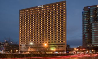 a tall , modern hilton hotel illuminated at night , with cars passing by in front of it at Hilton Lexington/Downtown