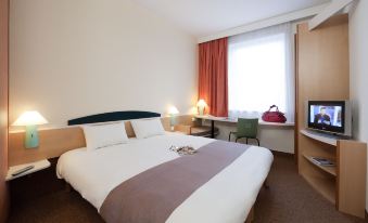a hotel room with a bed , desk , and window , giving a cozy and comfortable atmosphere at Ibis Luxembourg Sud