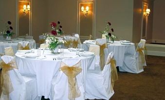 a well - decorated banquet hall with white tablecloths , gold chairs , and flowers on either side of the tables at Berlin Resort