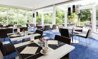 a modern restaurant with several tables and chairs , some of which are occupied by people at Novotel Maastricht