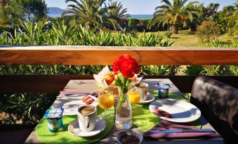 a table is set with breakfast items , including coffee cups and a flower , on a balcony overlooking palm trees at Mare E Monti