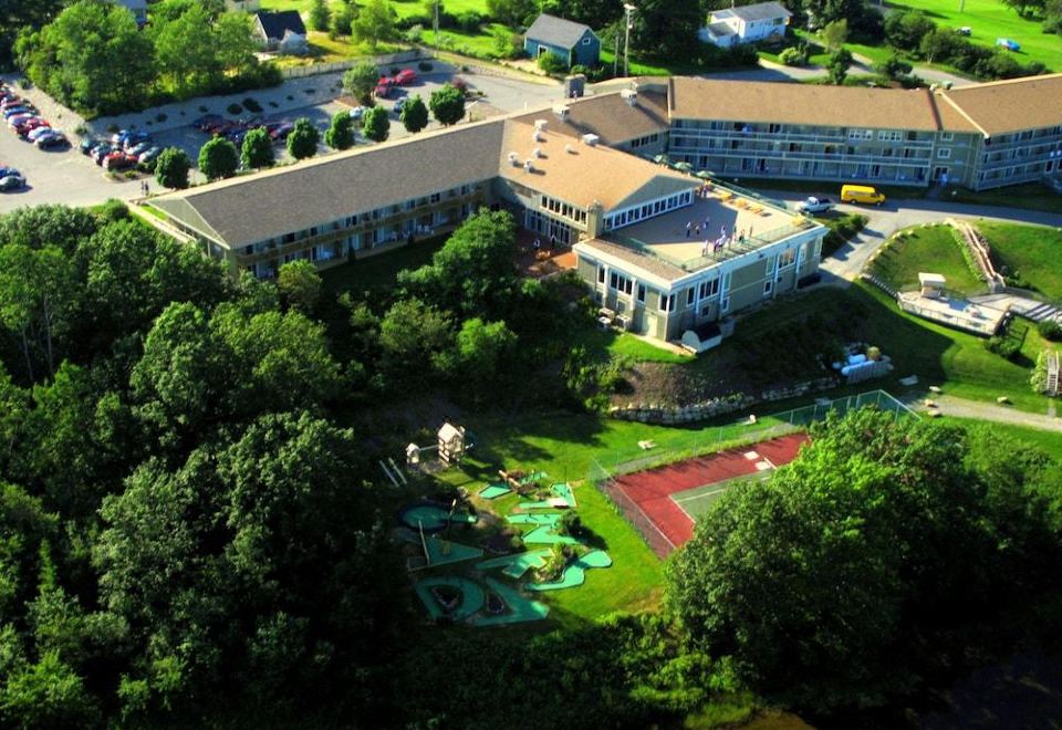 aerial view of a large hotel surrounded by trees and a park , with a tennis court in the foreground at Oak Island Resort & Conference Centre