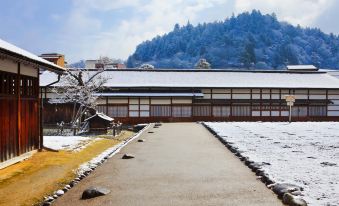 a snow - covered courtyard surrounded by a wooden building , with a tree in the background at Country Hotel Takayama
