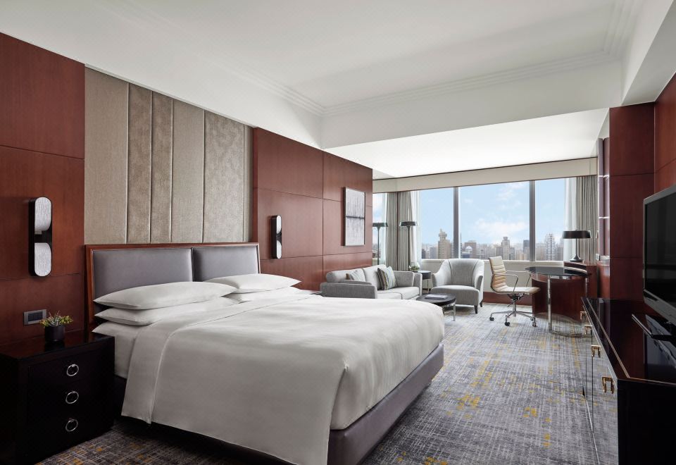 The room is furnished like an executive suite, featuring large windows, a bed, and a desk in the center at Shanghai Marriott Marquis City Centre
