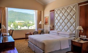 a large bed with a white headboard is in a room with a window and mountains visible outside at Islamabad Marriott Hotel