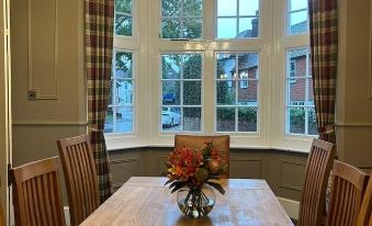 a wooden dining table with chairs and a vase of flowers in the center , surrounded by windows at The Ardingly Inn
