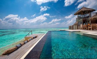 a large swimming pool is surrounded by a wooden deck and overlooks the ocean with a gazebo at Gili Lankanfushi Maldives