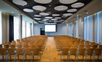 a large conference room with rows of wooden chairs arranged in a semicircle , and a projector screen mounted on the wall at Park Inn by Radisson Katowice