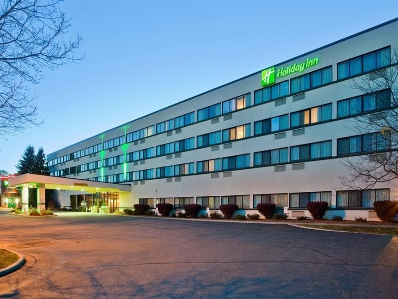 a large hotel building with a green sign on the side , located in a city setting at Holiday Inn Express Big Rapids